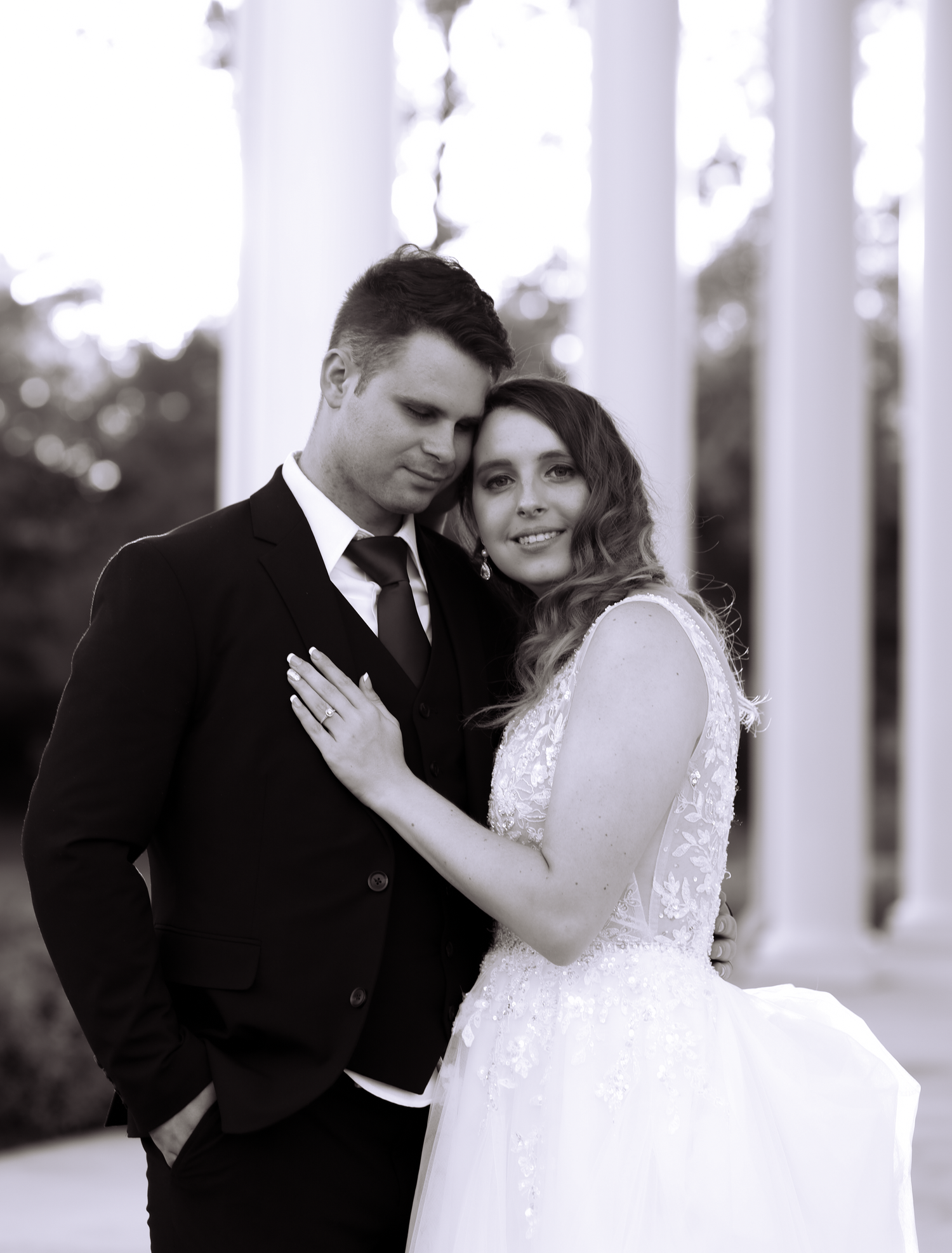 A classic black and white wedding photograph of newlyweds posing elegantly against white pillars in formal attire.