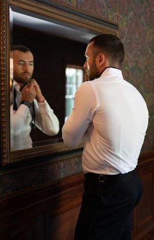 Person adjusting outfit in an ornate framed mirror with warm lighting.