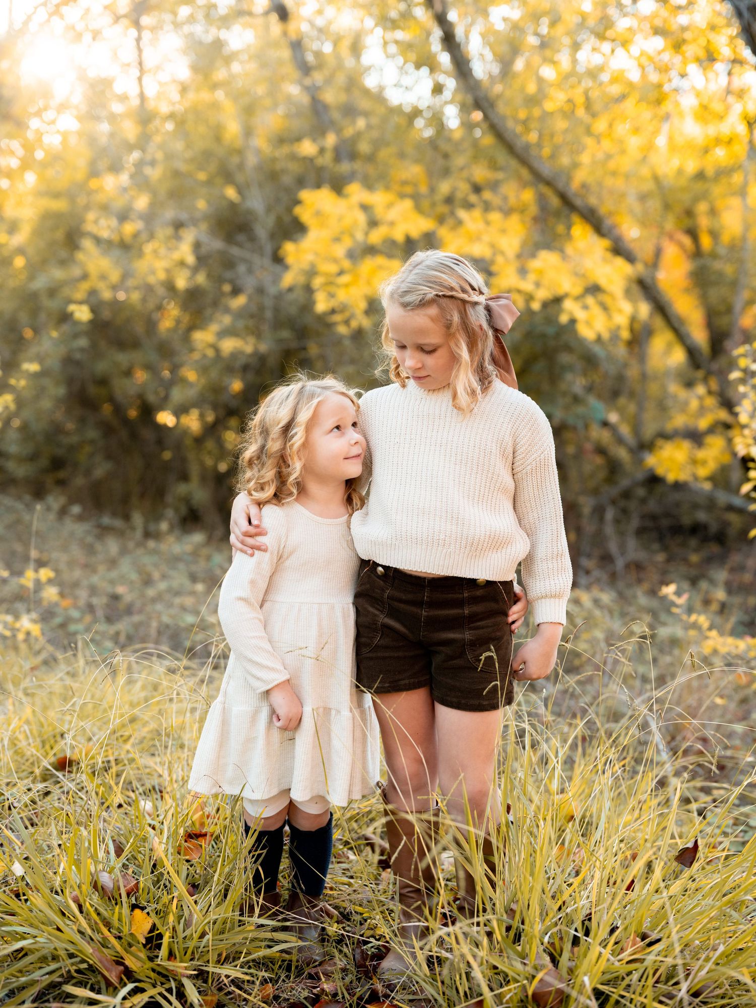 Family and brown dog pose together on autumn day with golden sunlit trees and fallen leaves in background.