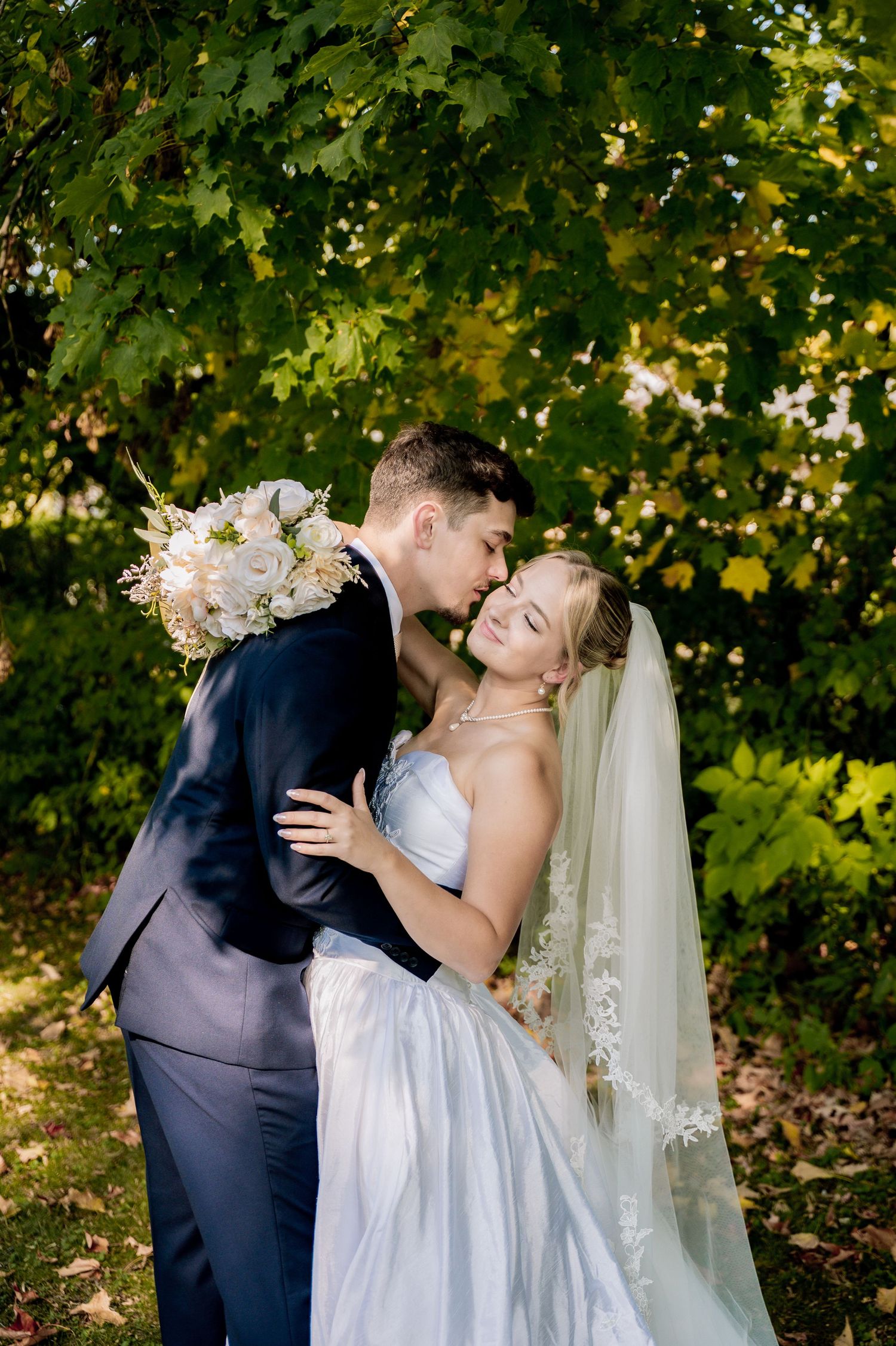 An outdoor wedding ceremony under a geometric arch draped with white fabric in a garden setting.