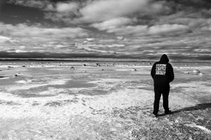 Solitary figure stands on snowy salt flats under dramatic black and white cloudy sky.