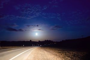 Full moon illuminates a deserted country road under a dramatic night sky.