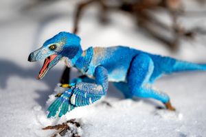Blue toy dinosaur figure positioned in snow with detailed scales and teeth.