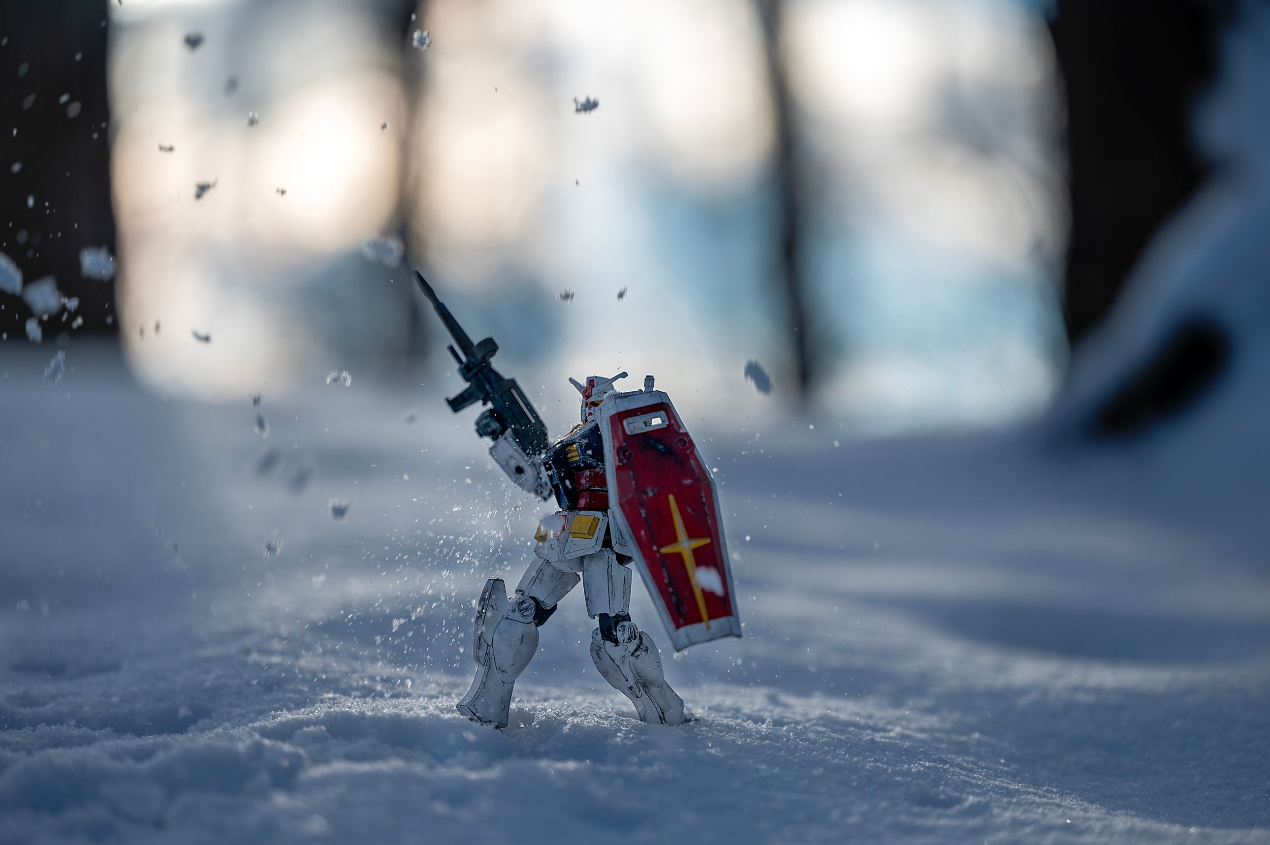 Gundam action figure posed dramatically in snow with flying particles.