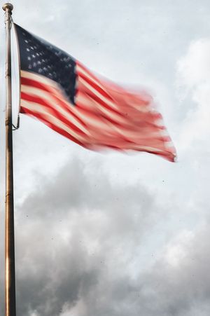 American flag waving dramatically in wind against stormy grey sky.