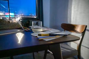 Study desk by window with laptop, papers and wooden chair in natural light.