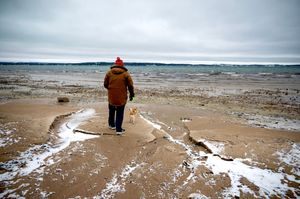 Person in brown coat walking on snowy beach during winter.