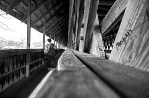 Black and white perspective shot down a wooden handrail in a covered bridge or walkway.