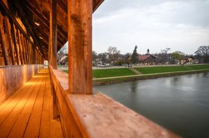 Wooden covered bridge walkway overlooking a calm river on a cloudy day.