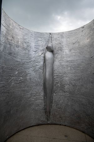 Abstract metal sculpture featuring a smooth vertical indentation in curved metallic surface.