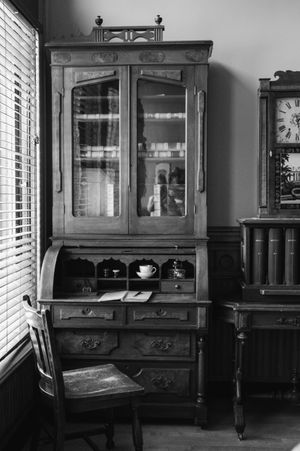 Vintage wooden secretary desk with glass cabinet doors and multiple drawers in black and white.