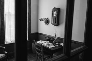 A dark and moody black and white interior hallway features vintage furniture and dramatic window lighting.
