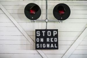 Vintage railroad crossing signal with red lights and black 'STOP ON RED SIGNAL' sign mounted on white wood wall.