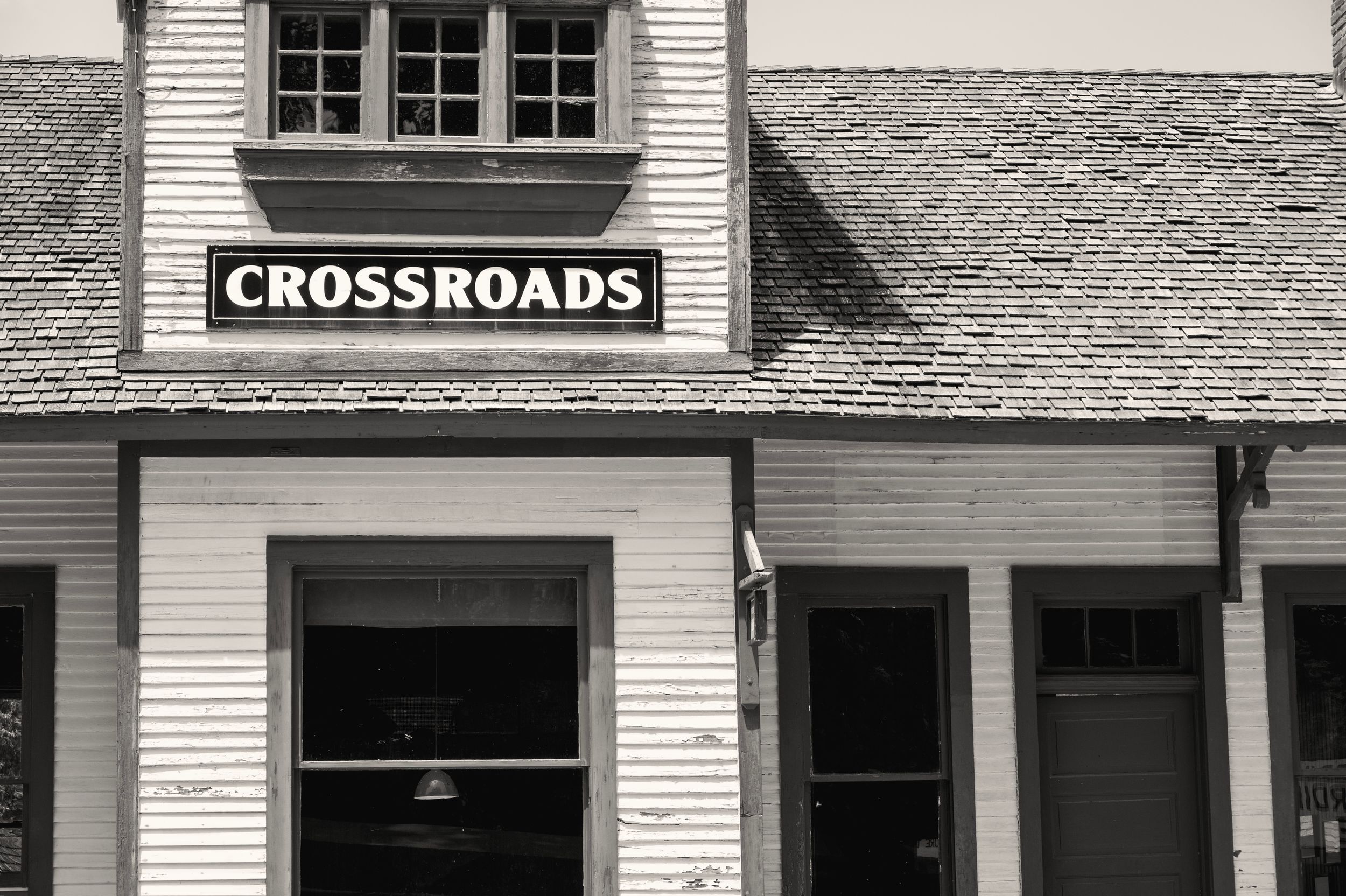 Black and white image of a building exterior with Crossroads sign mounted above storefront windows and doors.