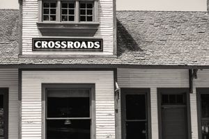 Black and white image of a building exterior with Crossroads sign mounted above storefront windows and doors.