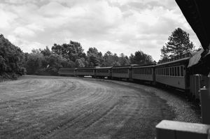 A black and white landscape photo shows a curving path through rolling hills with trees in the distance.