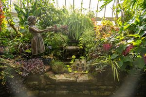 Lush garden terrace with stone walls features diverse tropical plants, flowers, and decorative landscaping elements.