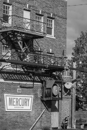 Vintage Mercury sign on brick building with fire escapes and clock mounted on exterior wall in black and white photograph.