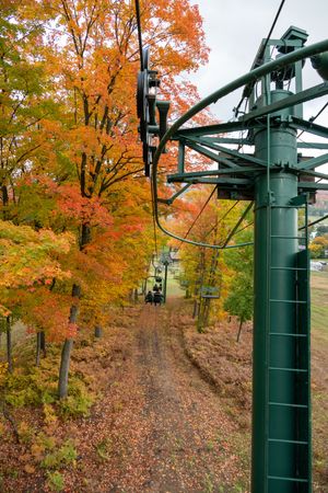 Ski lift towers stand against vibrant orange autumn foliage on a wooded hillside during fall season.