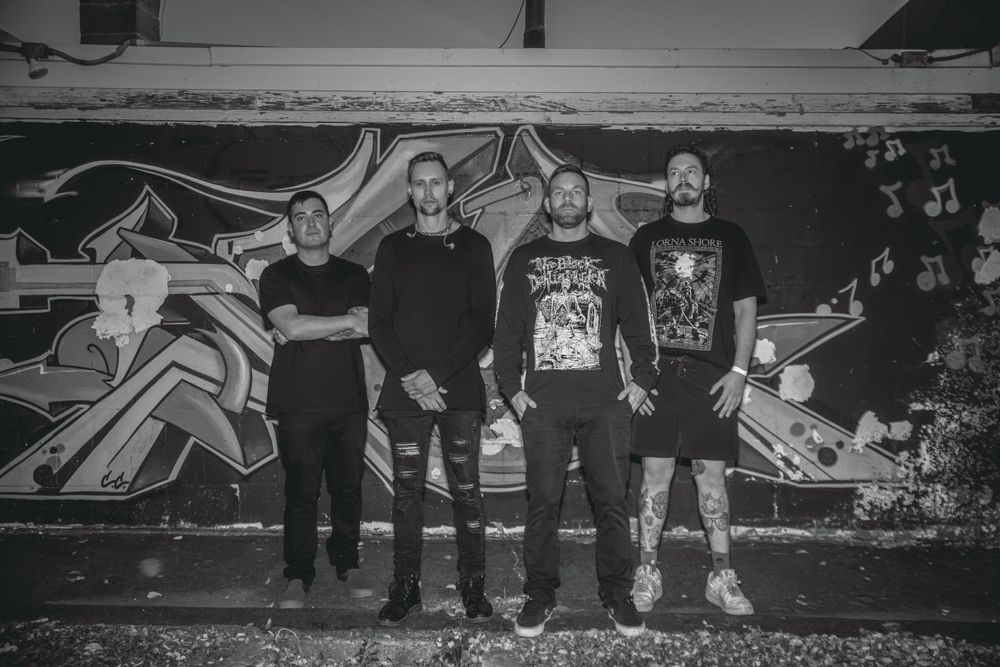 Black and white photo of group posing in front of graffiti wall.