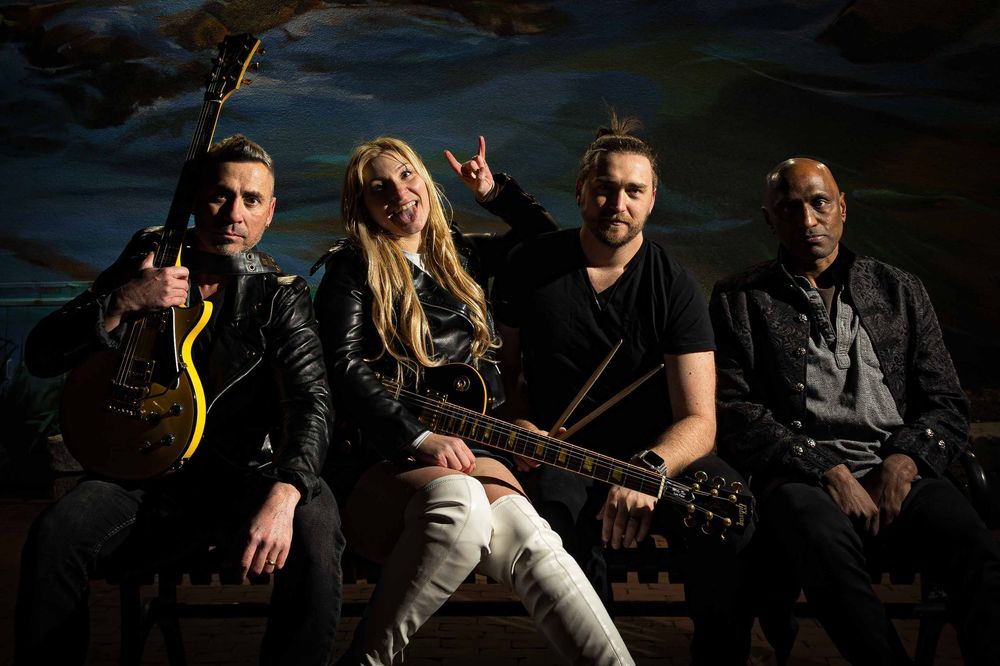 Rock band members posing with instruments against dramatic evening sky backdrop.