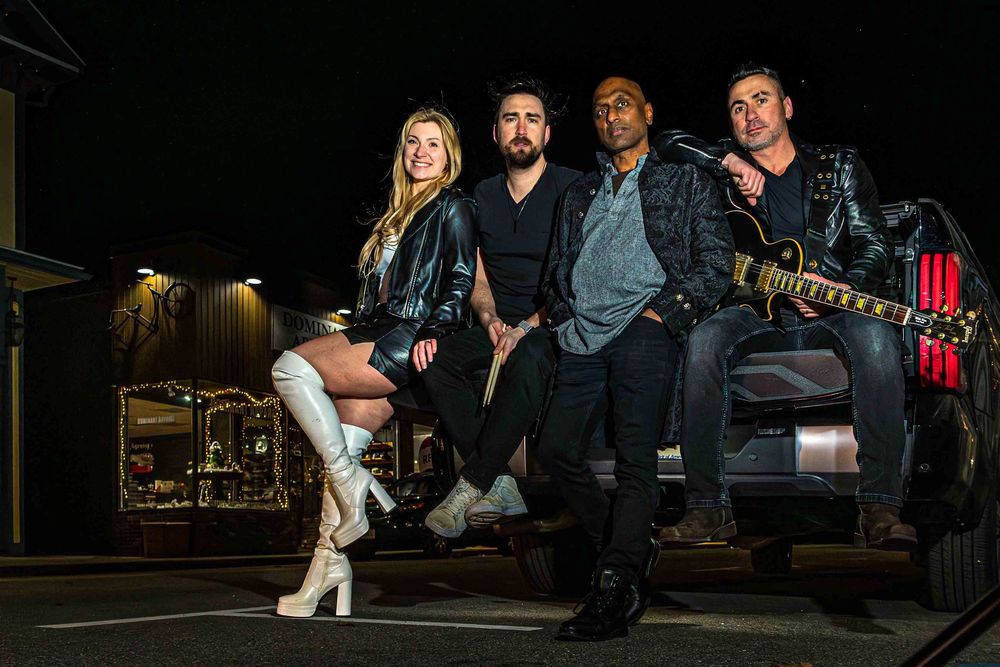 A band poses together against a dark background in a moody photoshoot setting.