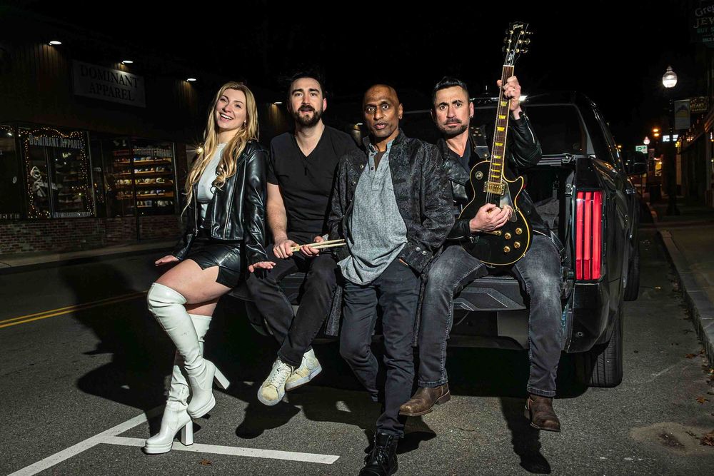Musicians gather for a group photo against an industrial backdrop.