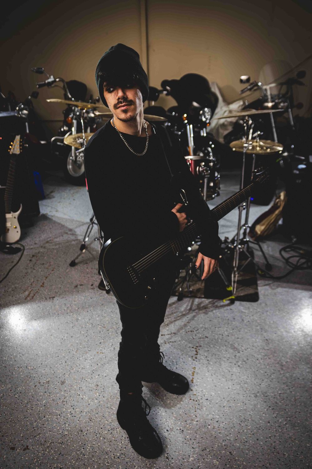 A musician crouches near drum equipment in a dimly lit studio space.