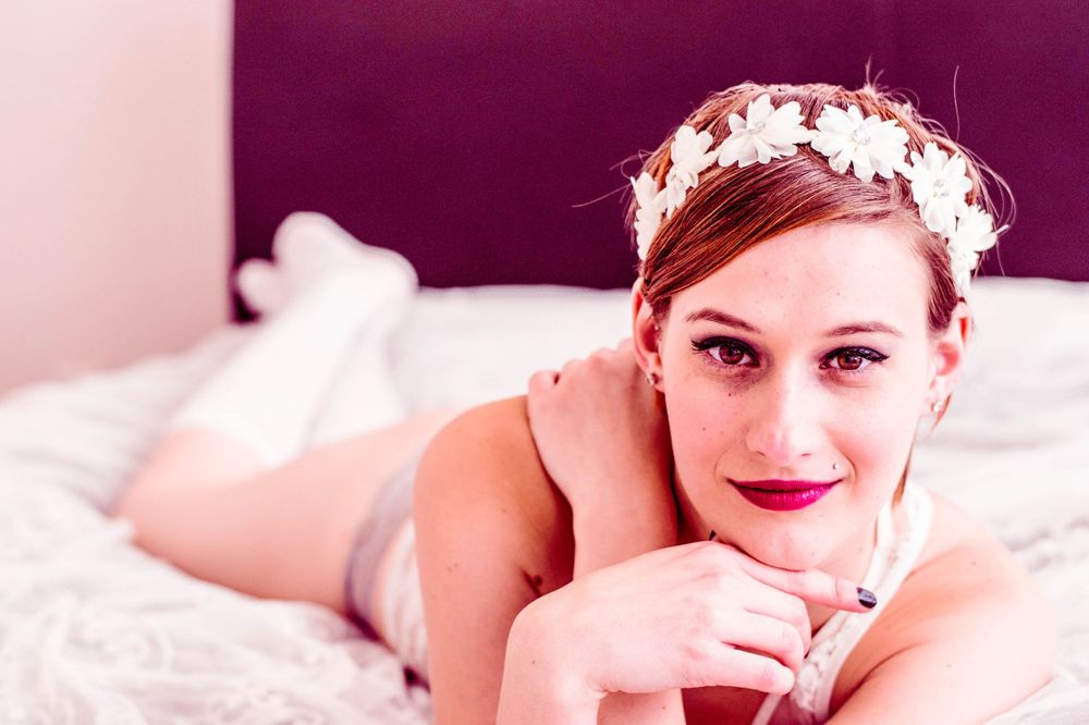 Vintage inspired boudoir photo with soft lighting and pearl crown headpiece on pink bedding.