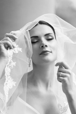 A dreamy black and white bridal portrait showing a serene expression beneath a delicate lace veil.