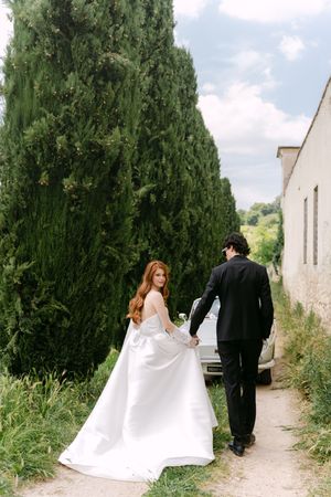 Sequence of four romantic wedding photos showing a couple walking along a stone path surrounded by tall cypress trees.