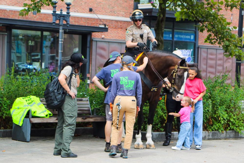 A mounted police officer interacts with visitors on a city street near a brick building.