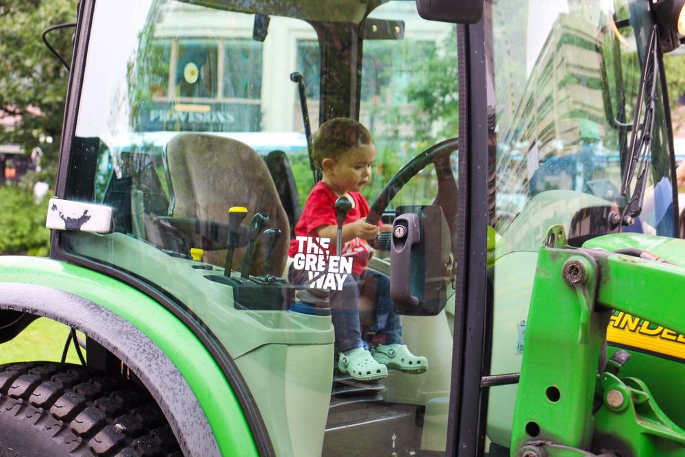 A young visitor sits in the driver's seat of a green tractor during an outdoor event.
