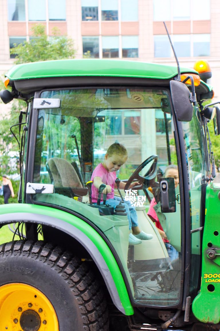 A visitor explores the interior of a bright green John Deere tractor cab.