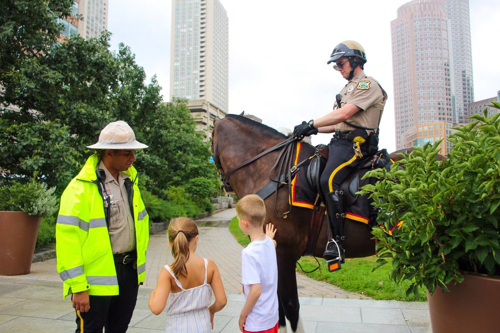 A mounted officer and safety personnel interact with visitors near urban buildings.