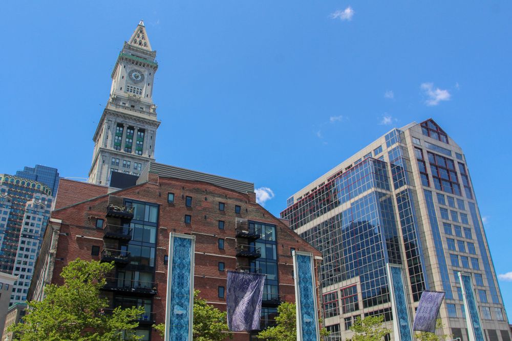 Historic Custom House Tower and modern buildings rise against blue sky in Boston.