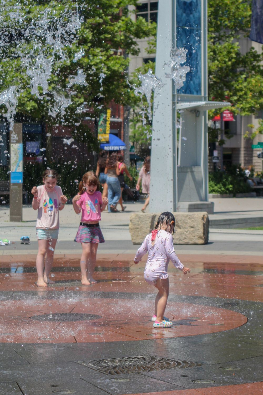 Children play in a public fountain splash pad on a sunny day.