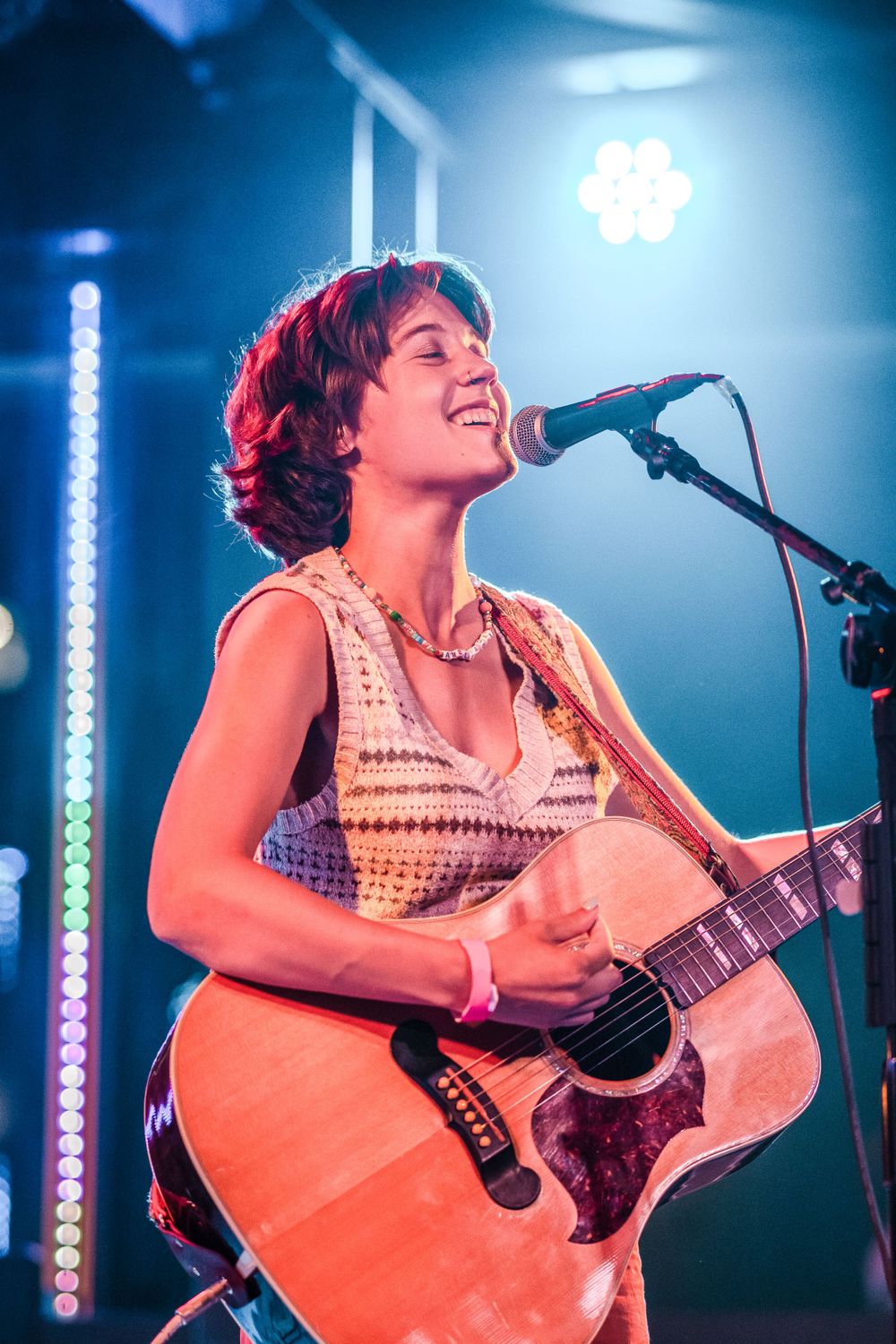 A musician performs on stage with an acoustic guitar under dramatic blue and red lighting.