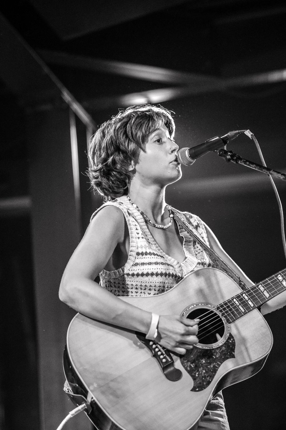 Black and white photo of a musician singing and playing acoustic guitar on stage.