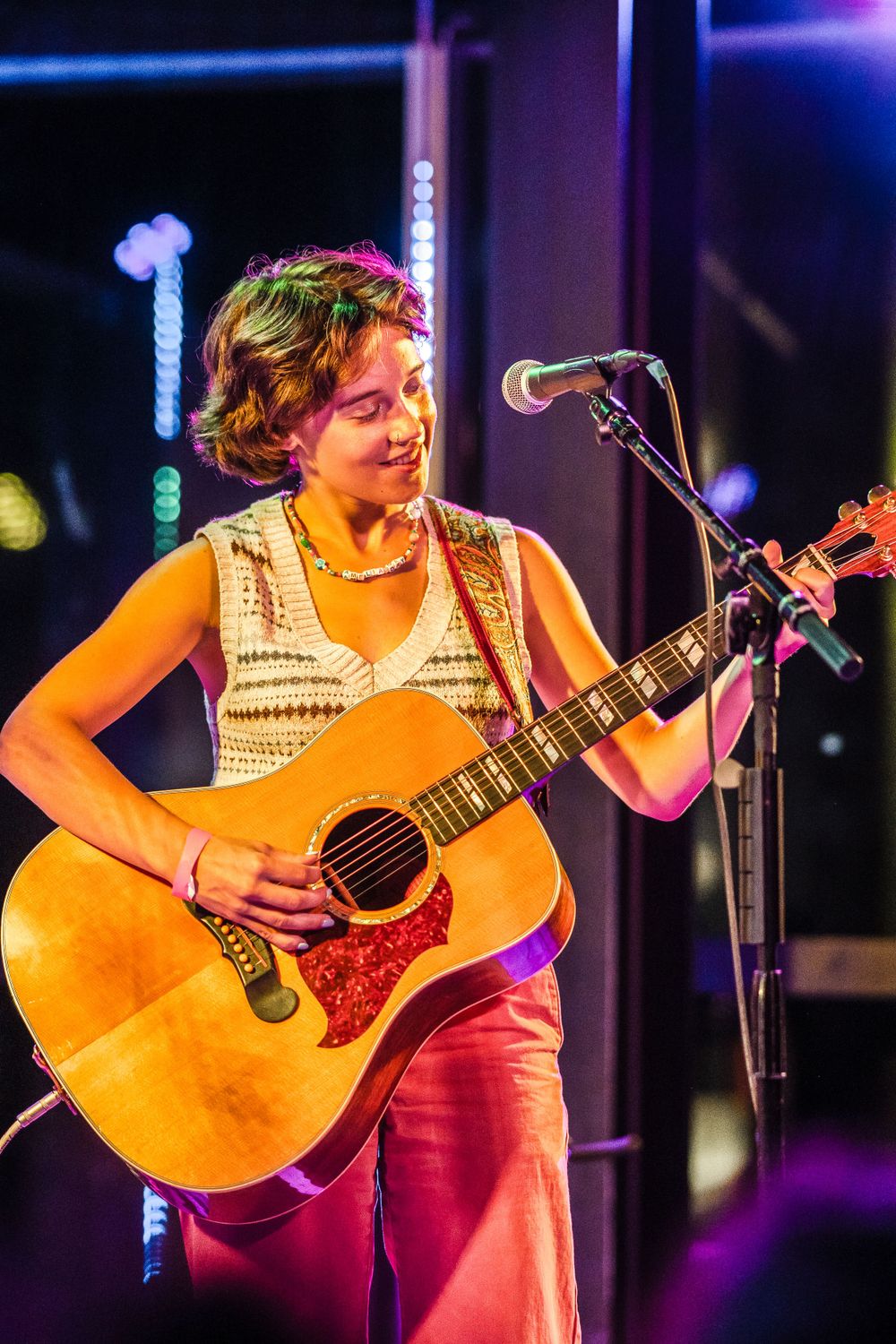 A musician performs with an acoustic guitar under colorful stage lighting.
