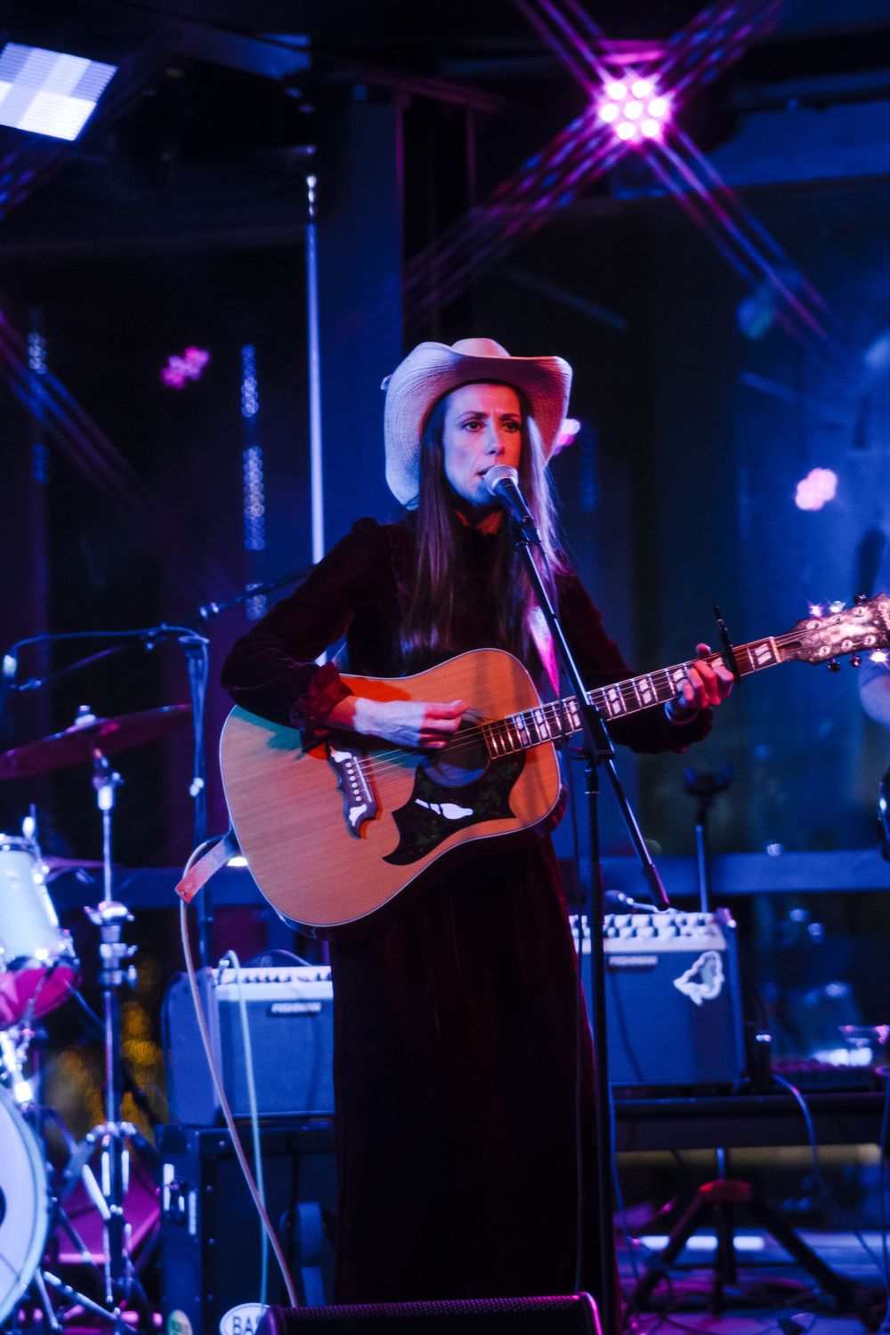 Country artist in cowboy hat performing with acoustic guitar on dimly lit stage.