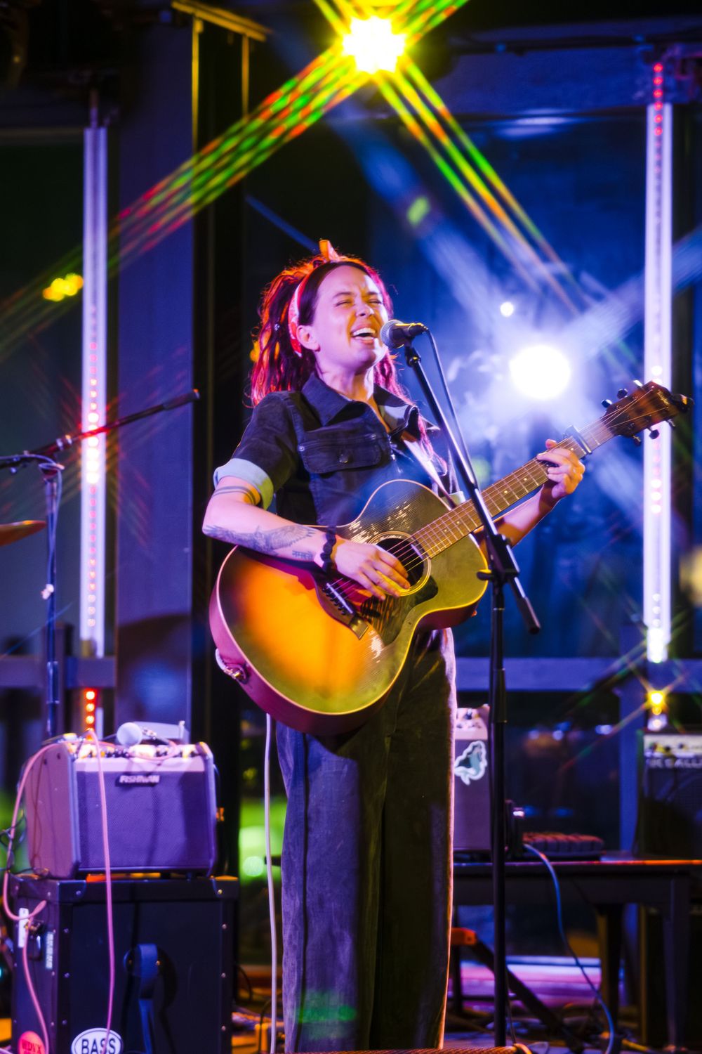Concert performer with acoustic guitar on stage illuminated by bright yellow spotlight.