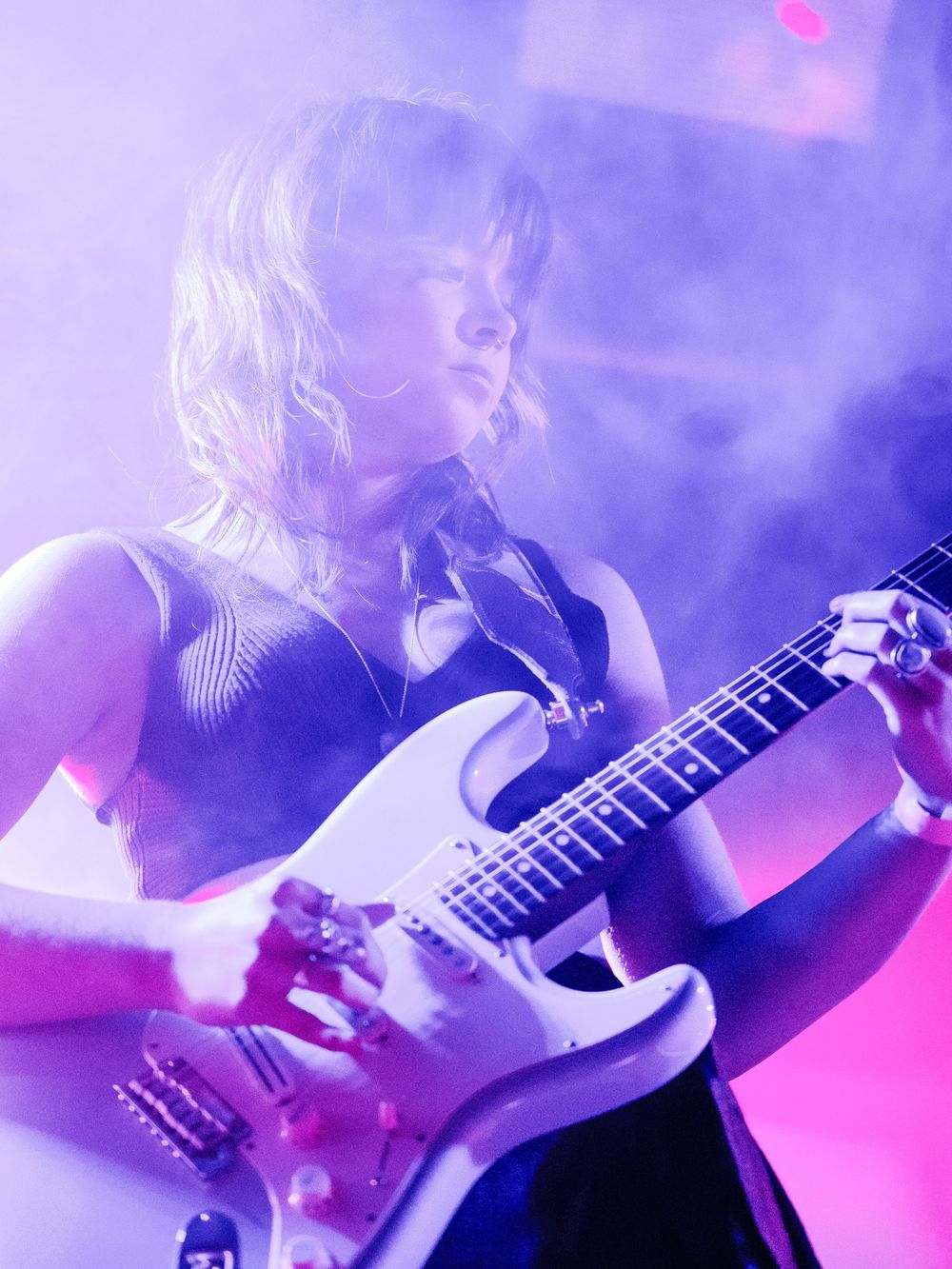 Guitarist playing electric guitar under purple stage lights during concert performance.
