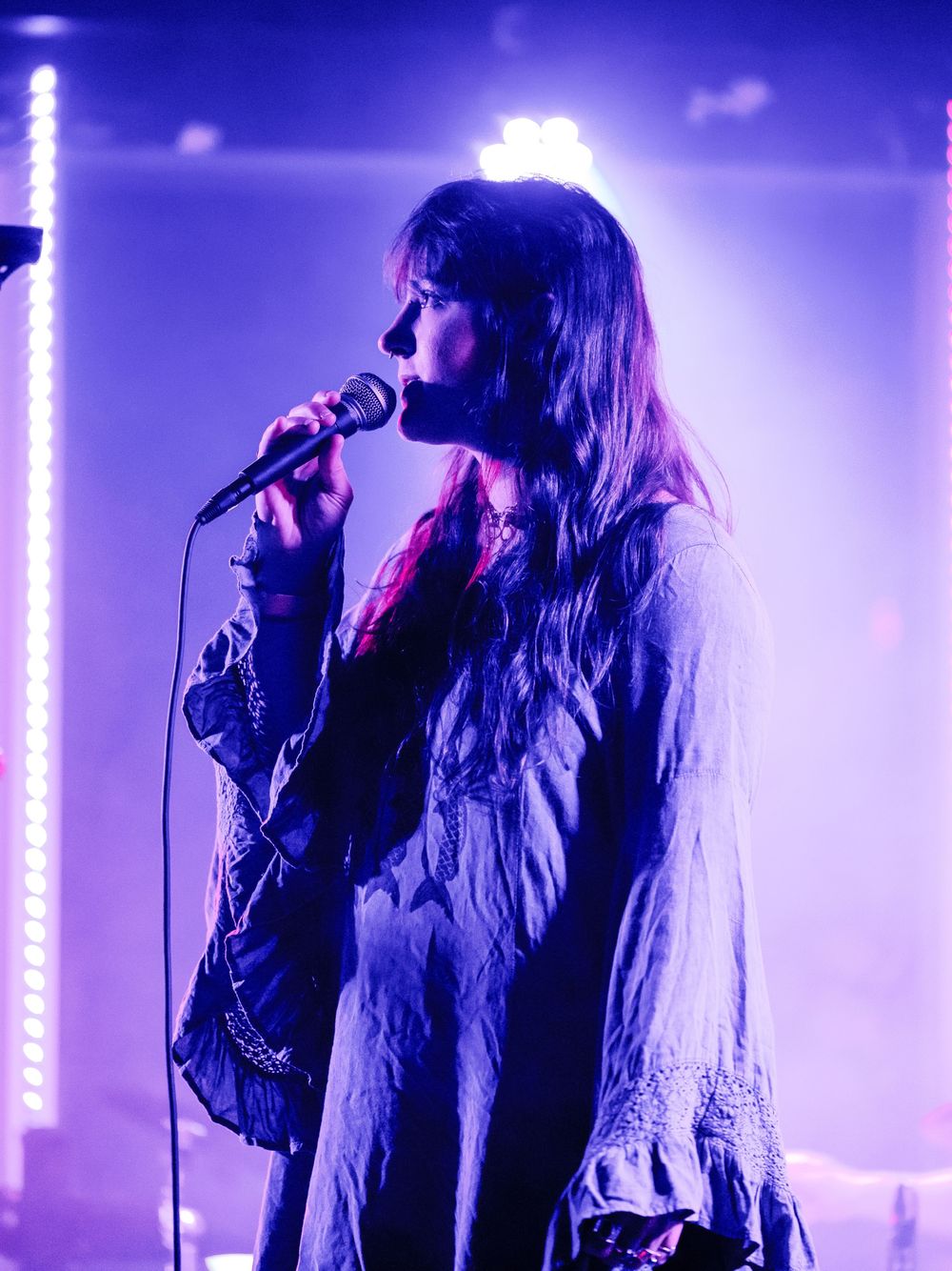 Singer performing on stage in ethereal blue lighting with long flowing hair and dark clothing.