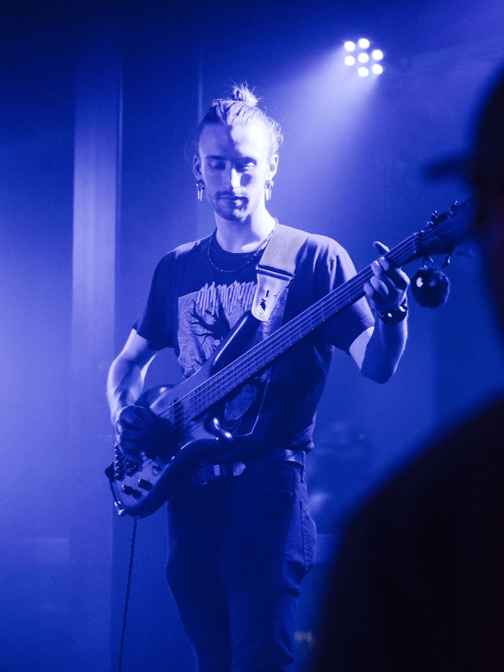 Musician playing bass guitar bathed in intense blue stage lighting.