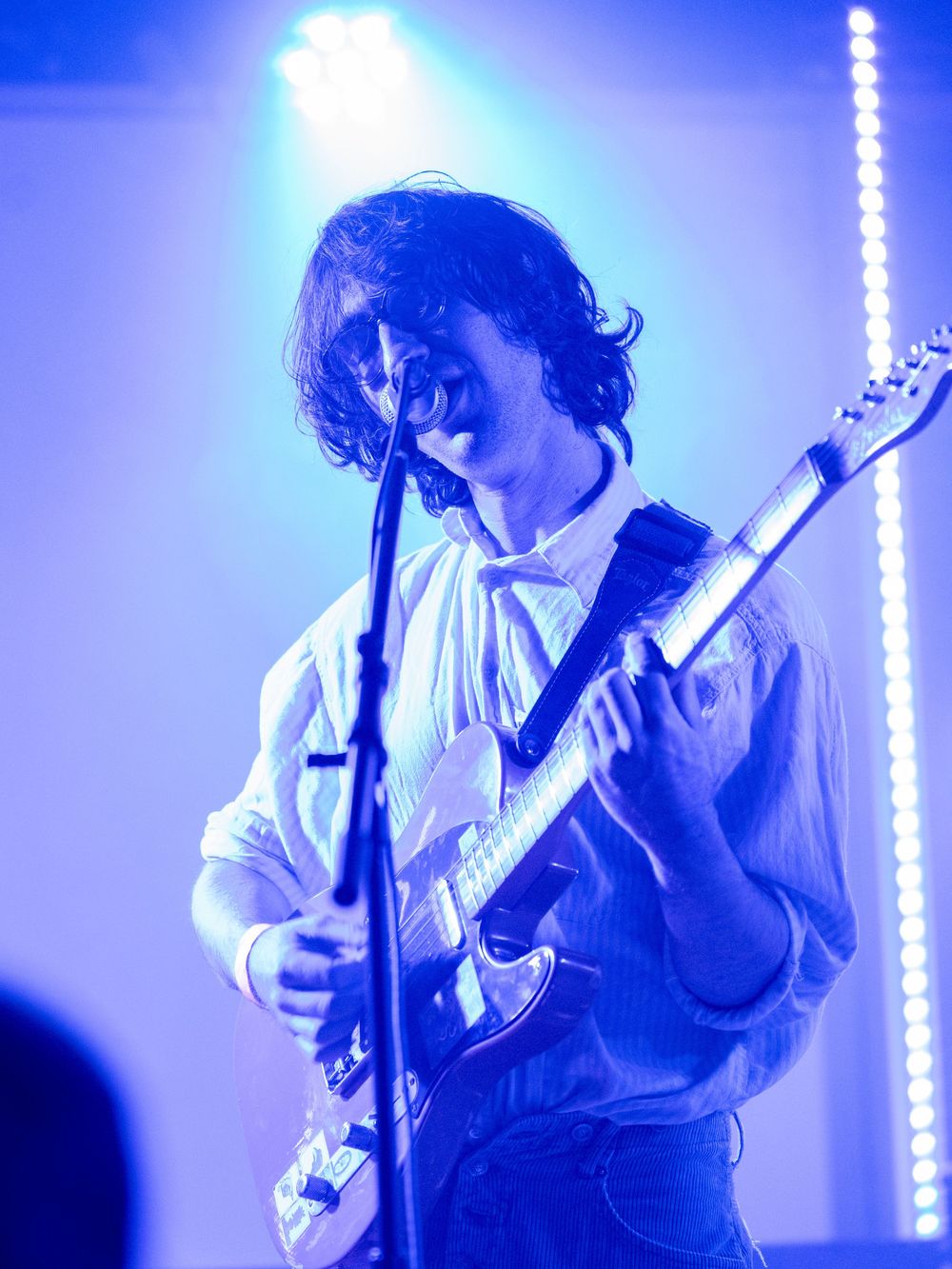 Guitarist in white shirt performing under dramatic blue stage lighting.