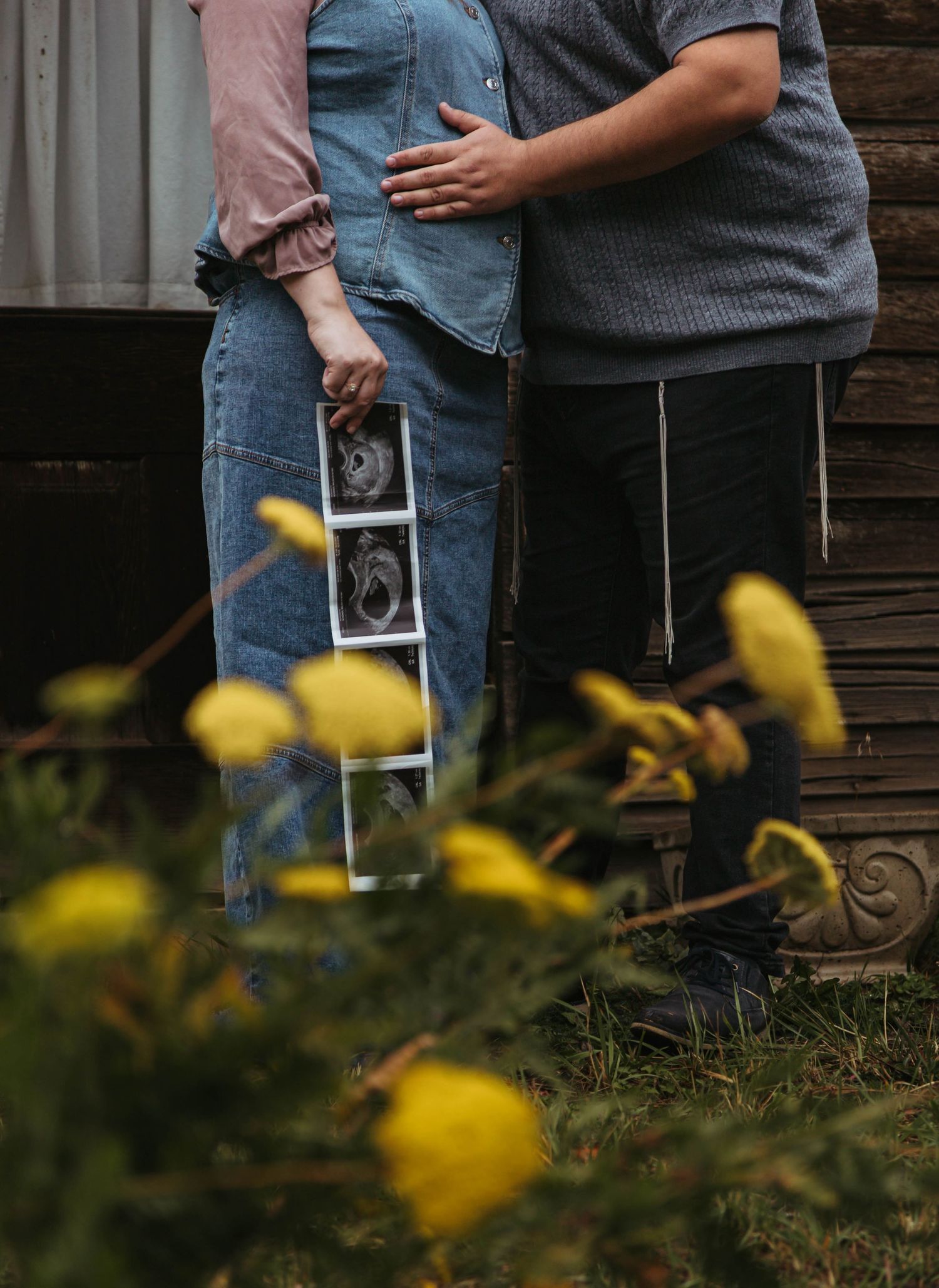 A tender maternity photo shoot in a garden with white umbrella and blooming lavender flowers in the foreground.