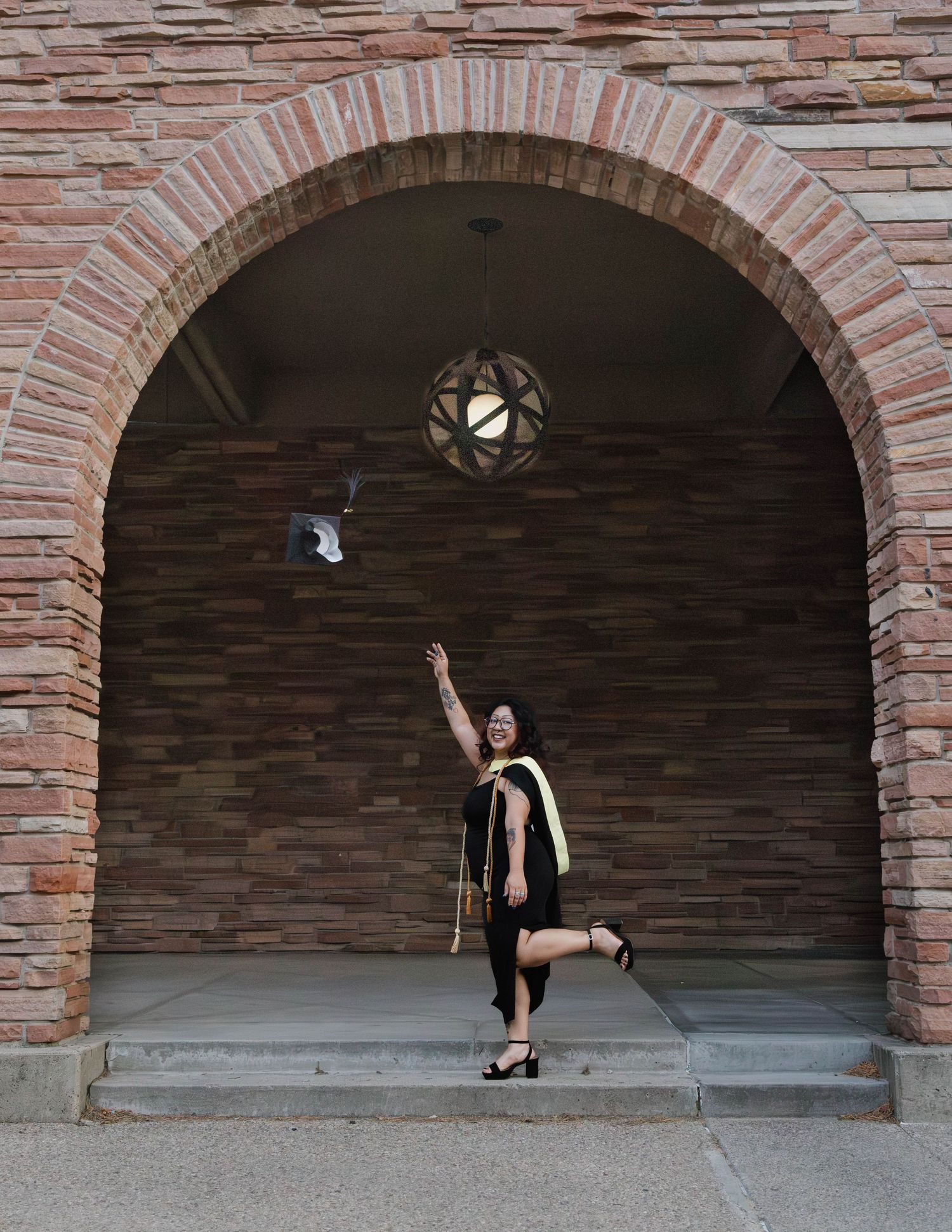 A dancer strikes a graceful pose under a brick archway with a decorative light fixture overhead.
