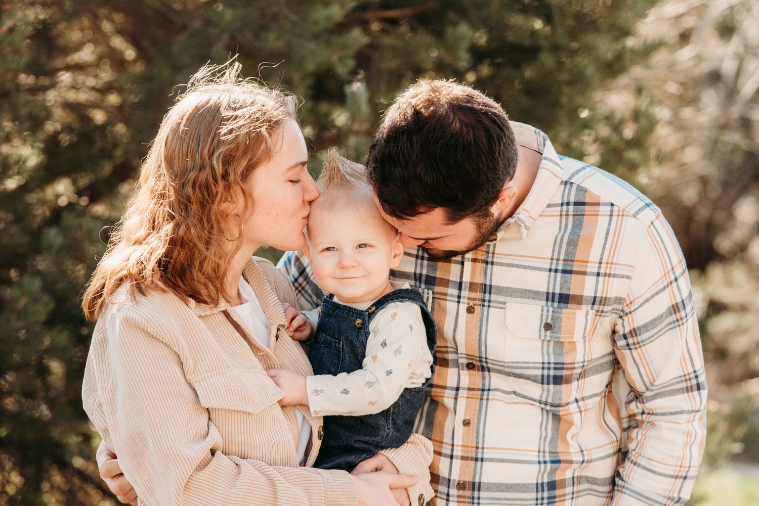 A tender family moment outdoors as parents share a sweet moment with their baby among winter trees.