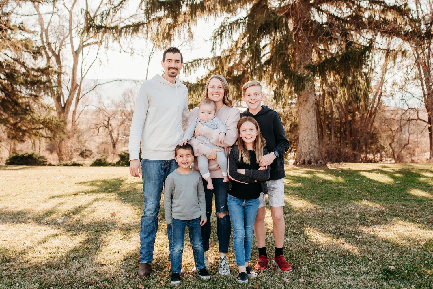 A small family group stands together under evergreen trees on a sunny autumn day.